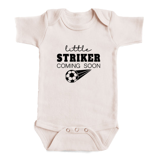 A baby onesie with the text "little STRIKER COMING SOON" printed on it, along with a soccer ball graphic.