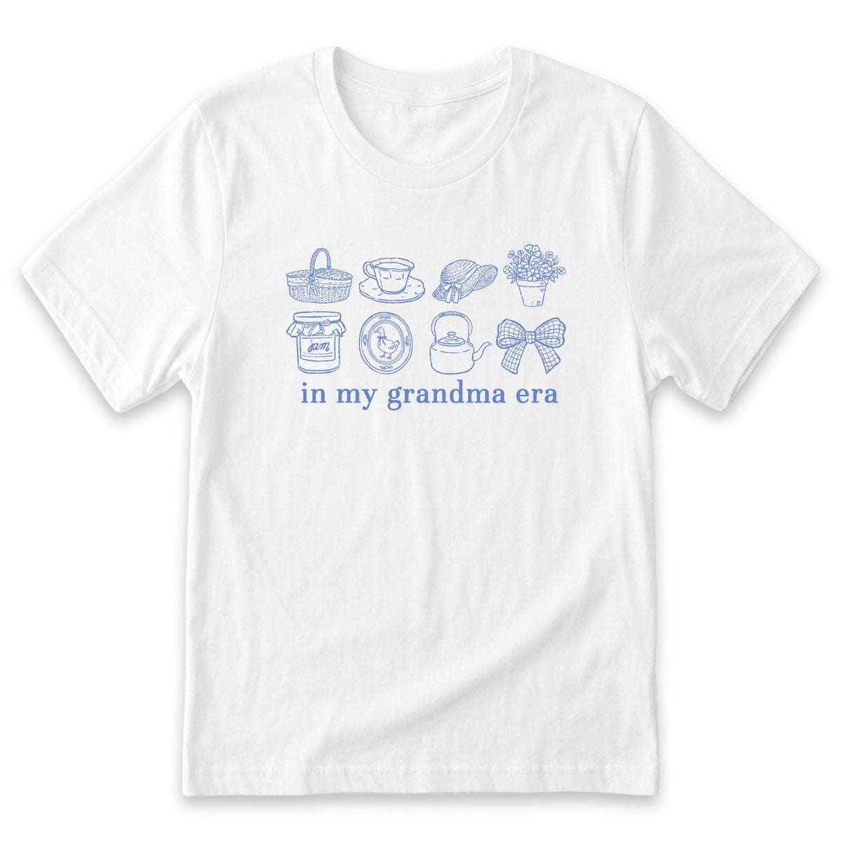 A white t-shirt with a graphic design featuring various objects such as a basket, teapot, cup, and flowers, along with the text "in my grandma era" printed on it.