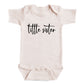 A baby onesie with the text "tittle sister" printed on it.