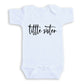 A white baby onesie with the text "title sister" printed on it.