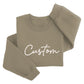 A beige sweatshirt with the word "Custom" printed on it in white cursive text.