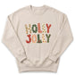 A beige sweater with the text "HOLY JOY" printed on it in a festive, holiday-themed font.