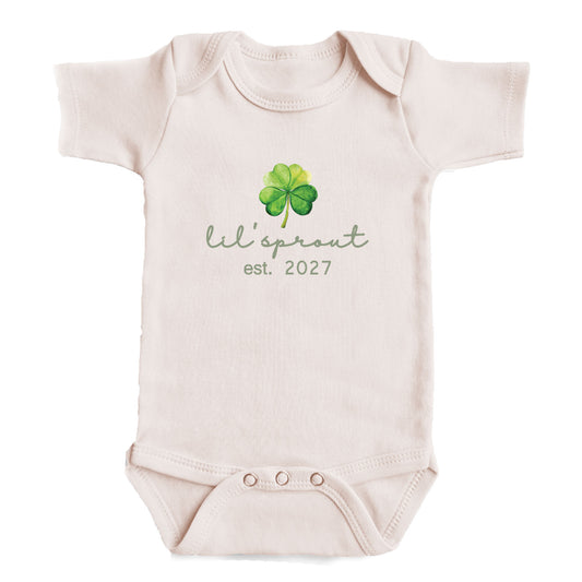 A baby onesie with a cloverleaf design and the text "Lil' sprout est. 2027" printed on it.
