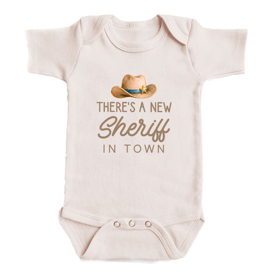 a baby onesie with a cowboy hat and the text "There's a new Sheriff in town" printed on it.
