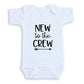 A white baby onesie with the text "NEW to the CREW" printed on it.