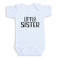 A white baby onesie with the text "Little Sister" printed on it.