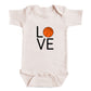 A white baby onesie with the word "LOVE" printed on it, featuring an orange basketball graphic.