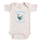 A baby onesie with a printed design of a whale and the text "Whalecome to the world" on it.