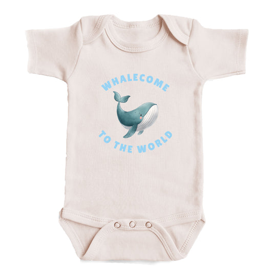 A baby onesie with a printed design of a whale and the text "Whalecome to the world" on it.