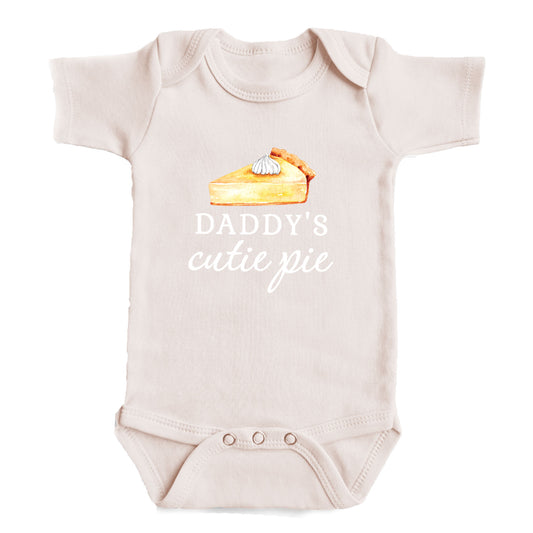 A baby onesie with a printed design of a slice of pie and the text "DADDY'S CUTIE PIE" printed on it.