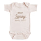 A baby onesie with the text "BABY Laney April 2027" printed on it.