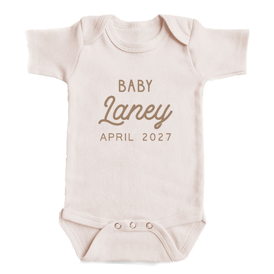 A baby onesie with the text "BABY Laney April 2027" printed on it.