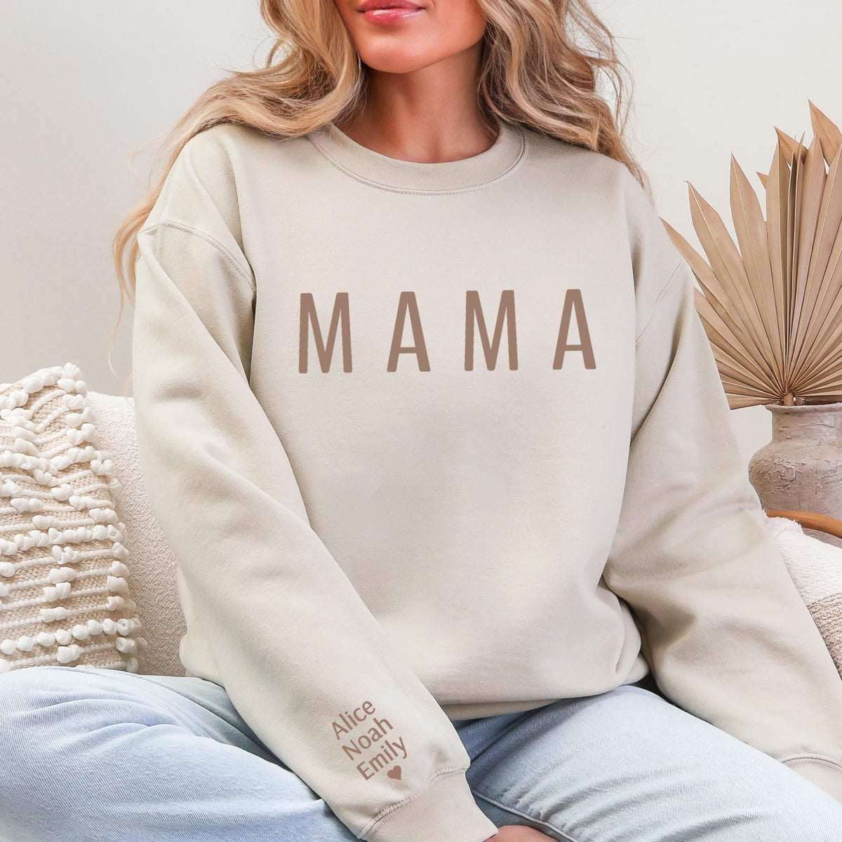 A woman wearing a beige sweatshirt with the word "MAMA" printed on it, sitting on a couch.