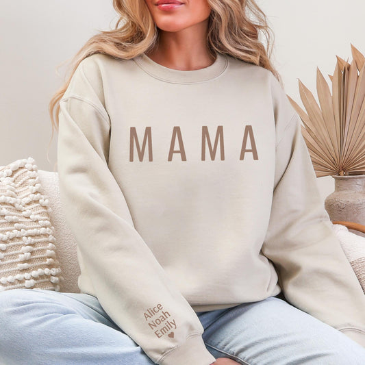 A woman wearing a beige sweatshirt with the word "MAMA" printed on it, sitting on a couch.