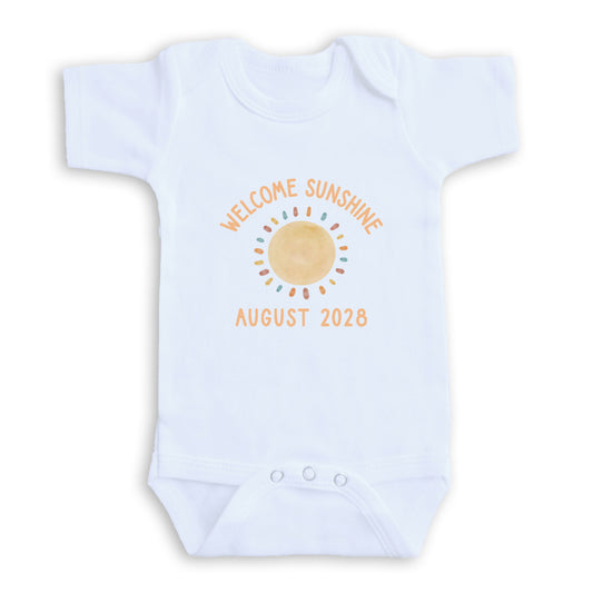 A white baby onesie with a sun graphic and text that reads "Welcome sunshine August 2028".