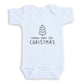 A white baby onesie with a Christmas tree graphic and the text "COMING HOME FOR CHRISTMAS" printed on it.