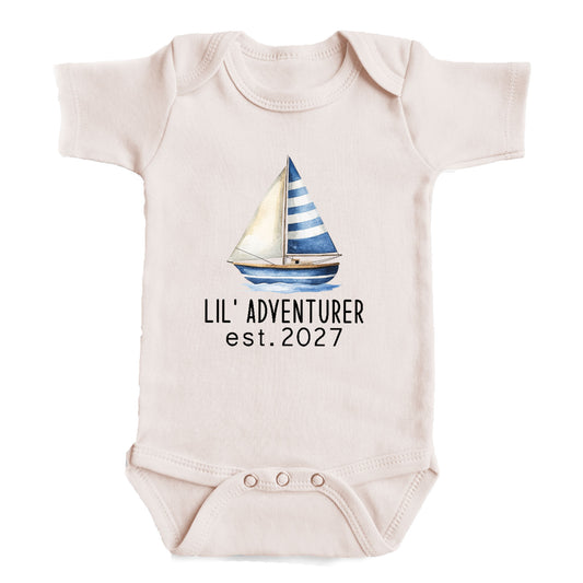A baby onesie with a sailboat printed on it, and the text "LIL' ADVENTURER est. 2027" printed below the sailboat.