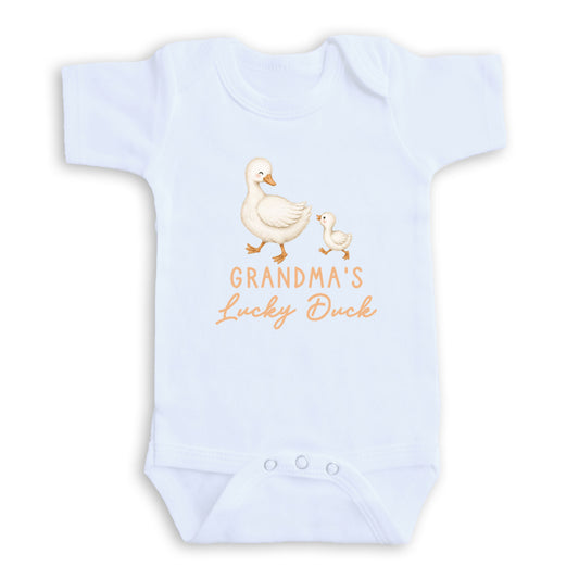 A white baby onesie with a graphic design of two ducks, one larger and one smaller, along with the text "GRANDMA'S Lucky Duck".