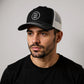 A man wearing a black baseball cap with a white logo on it.