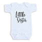 A white baby onesie with the text "Little Sister" printed on it.