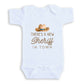 A white baby onesie with a cowboy hat and text printed on it.