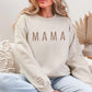 A woman wearing a beige sweatshirt with the word "MAMA" printed on it, sitting on a couch.