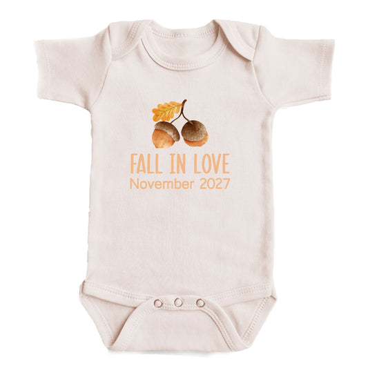 A baby onesie with an acorn and leaf design, along with the text "FALL IN LOVE November 2027".