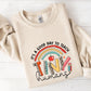 A beige sweatshirt with a colorful graphic design on it, which says "It's a good day to teach tiny humans".