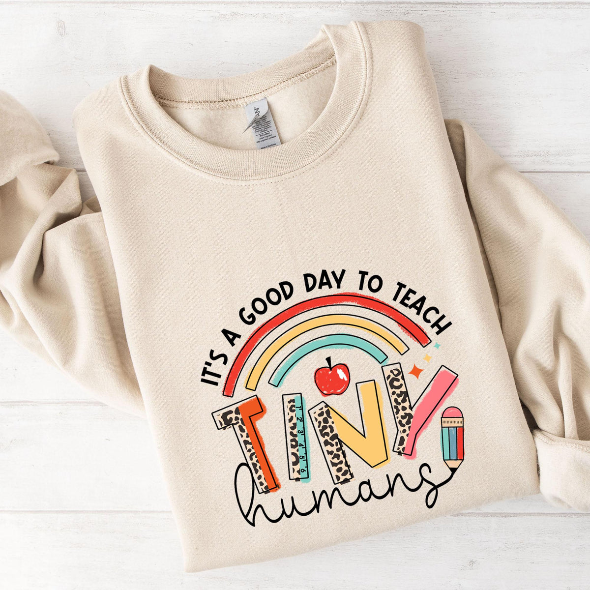 A beige sweatshirt with a colorful graphic design on it, which says "It's a good day to teach tiny humans".