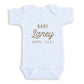 A white baby onesie with the text "BABY Laney April 2027" printed on it.