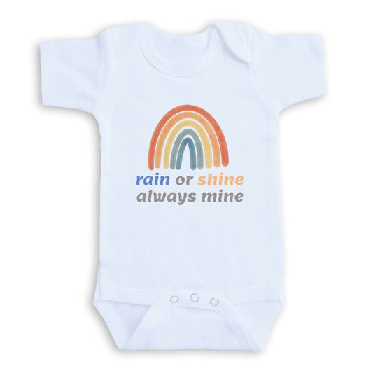 A white baby onesie with a rainbow graphic and the text "rain or shine always mine" printed on it.
