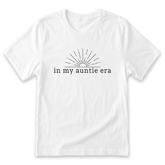A white t-shirt with a graphic design featuring a sun with rays emanating from it, accompanied by the text "in my auntie era" printed on it.