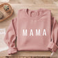 A pink sweatshirt with the word "MAMA" printed on it, placed on a wooden surface alongside a small potted plant and some papers.