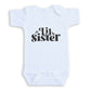A white baby onesie with the text "Lil Sister" printed on it.