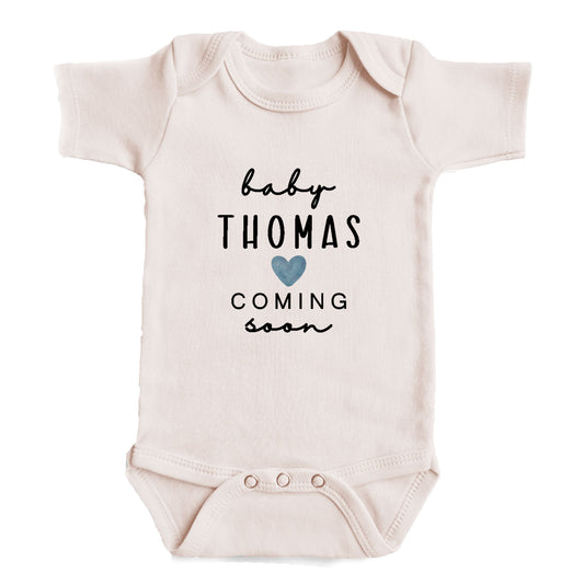 A baby onesie with the text "baby Thomas coming soon" printed on it.