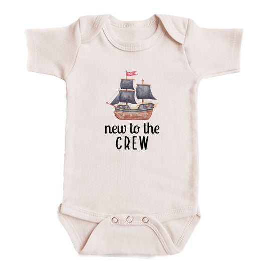 A baby onesie with a printed image of a pirate ship and the text "new to the crew" printed on it.