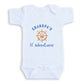 A white baby onesie with a graphic of a ship's steering wheel and the text "GRANDPA'S lil' adventurer" printed on it.