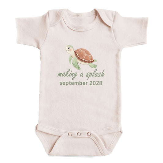 A baby onesie with a turtle graphic and the text "making a splash september 2028" printed on it.