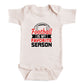 A white baby onesie with a printed text that says "Football is my favorite season" in black and red lettering.